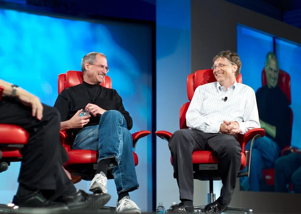 Bill Gates and Steve Jobs sitting across from one another, smiling.